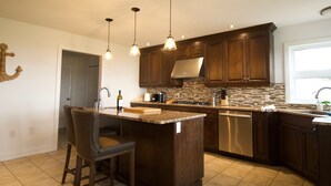 Cocina con armarios de madera oscura, una isla central con taburetes de bar, iluminación colgante y un lavavajillas de acero inoxidable.