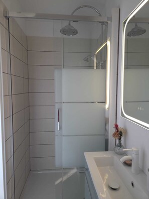 Ein modernes Badezimmer mit einer begehbaren Glasdusche, einem weißen Waschbecken und einem großen Spiegel.