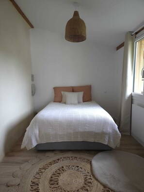 Ein Schlafzimmer mit einem Bett, einer gewebten Pendelleuchte und einem runden Teppich.