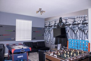 Una habitación con una mesa de fútbol de mesa, un sofá, un televisor instalado en la pared y un mural con temática de Star Wars.