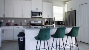 A modern kitchen with white cabinets, a microwave, a refrigerator, and a bar area with green chairs.