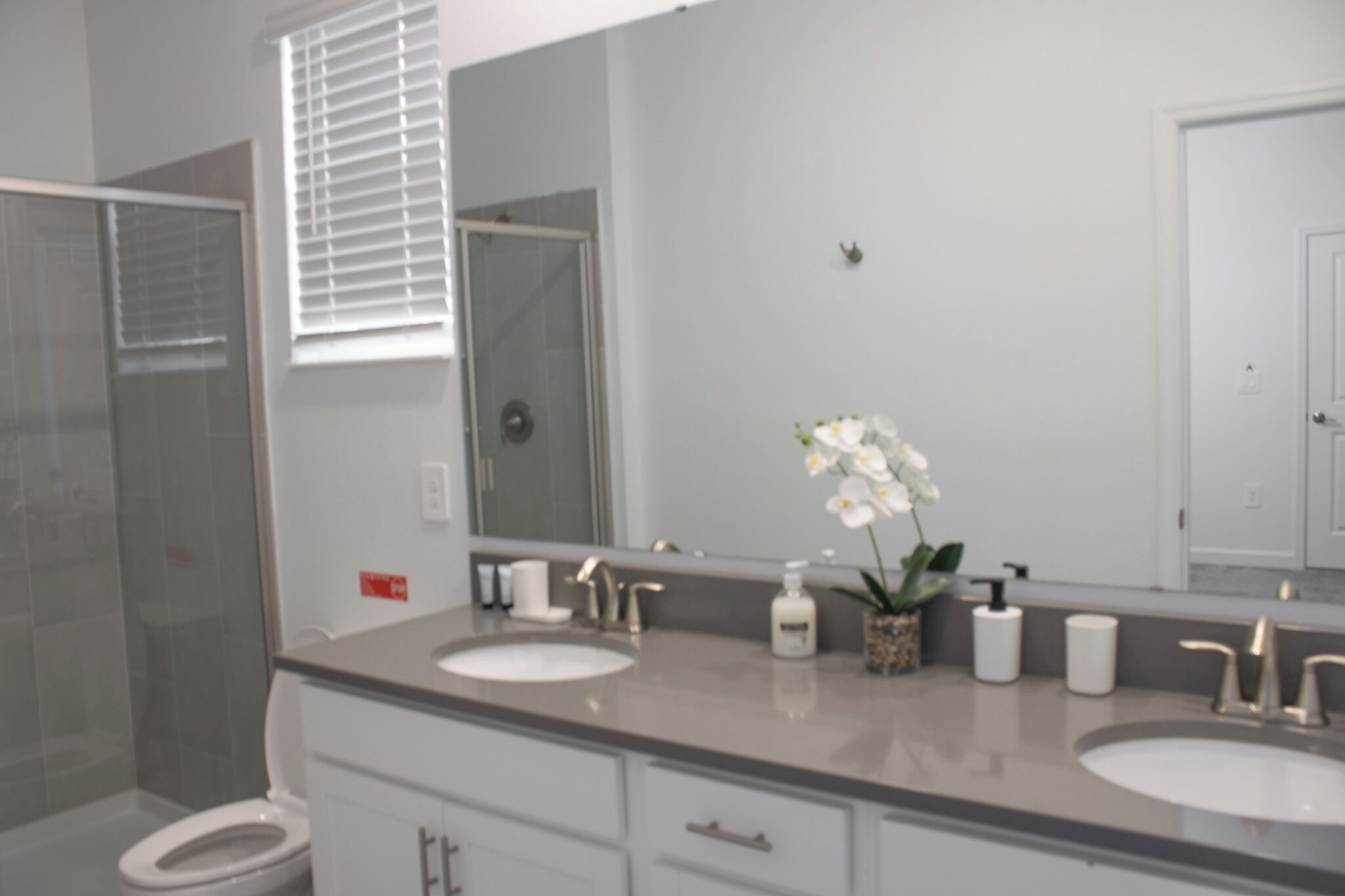 A bathroom with two sinks, a large mirror, a shower, and a toilet.