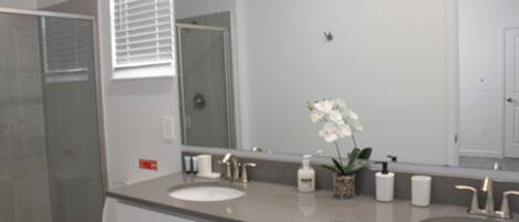 A bathroom with two sinks, a large mirror, a shower, and a toilet.
