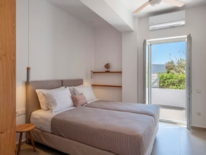 Ein modernes Schlafzimmer mit Bett, Nachttischen, Deckenventilator und Blick durch eine Glastür.