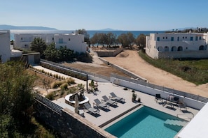 Ein Pool auf dem Dach mit Liegestühlen, Blick auf das Meer und weiße Gebäude im Hintergrund.