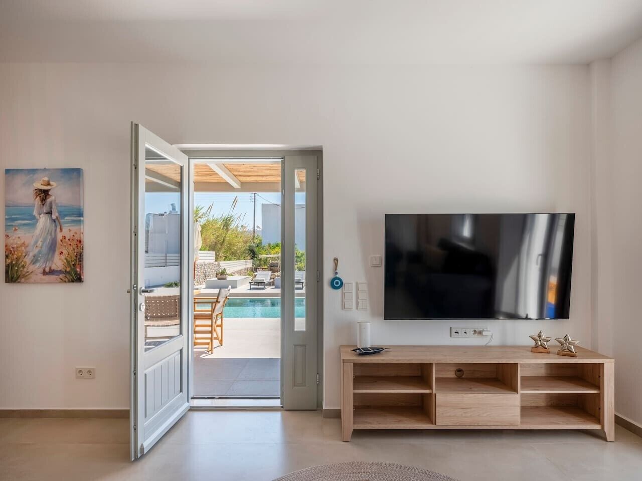 Una puerta abierta que da a una zona de piscina, un televisor de pantalla plana sobre un soporte de madera, y un cuadro en la pared.