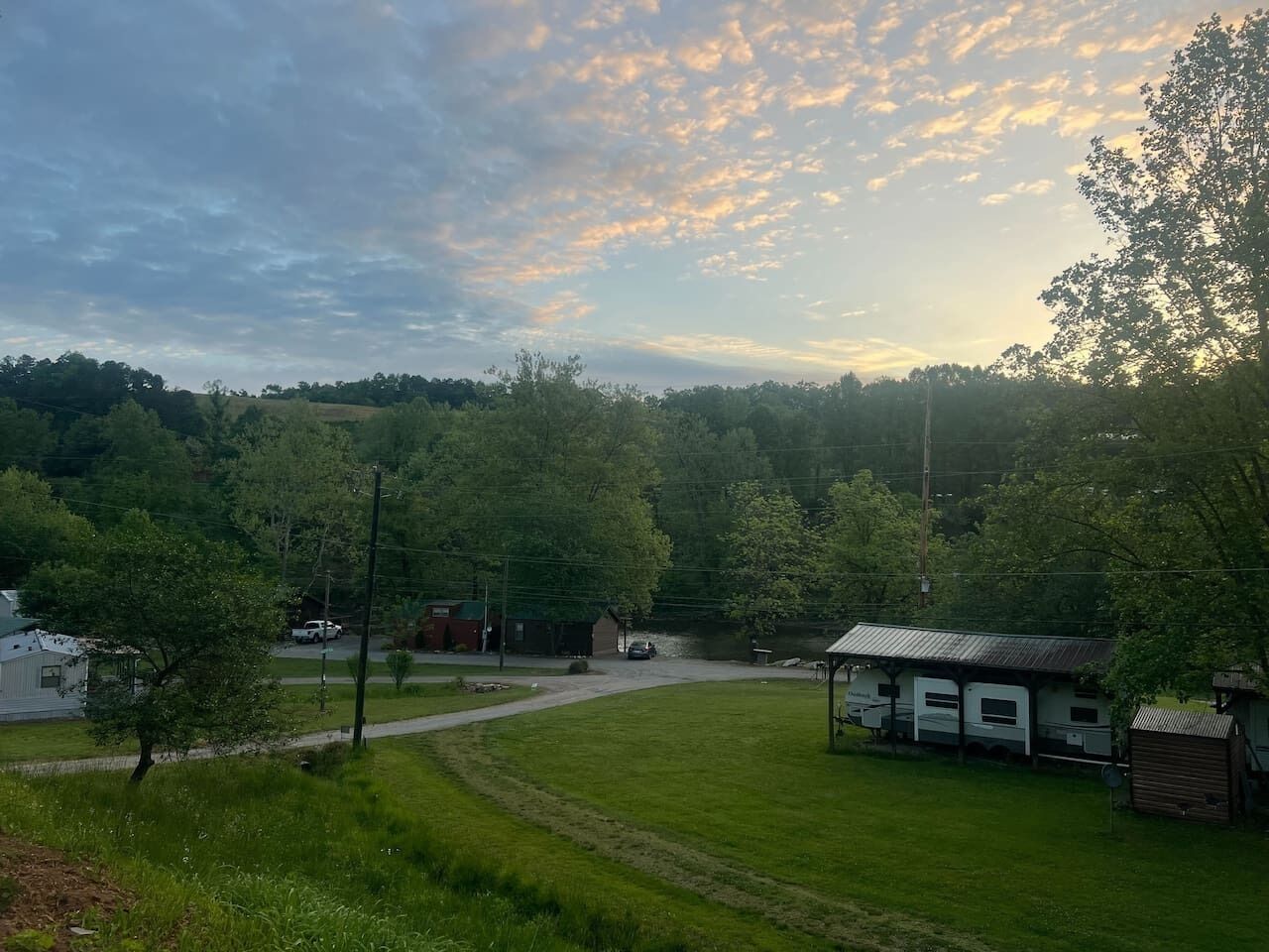 A rural landscape with a small cabin, a trailer, and a road.