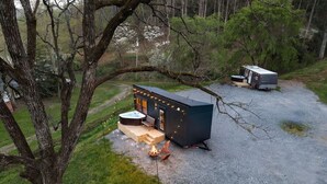 A small cabin with a hot tub and outdoor seating, surrounded by trees.