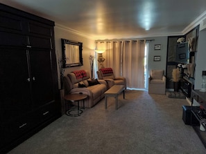 A living room with a sofa, armchair, and ottoman, a dark wooden cabinet, and a fireplace. - 1-bedroom condo in delightful, Arcadia area, Phoenix, AZ w/AC (Phoenix)