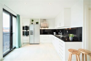 A modern kitchen with white cabinets, stainless steel appliances, a black countertop, and wooden stools. - Lodge Apartment in Centre of Antwerp (Antwerp)