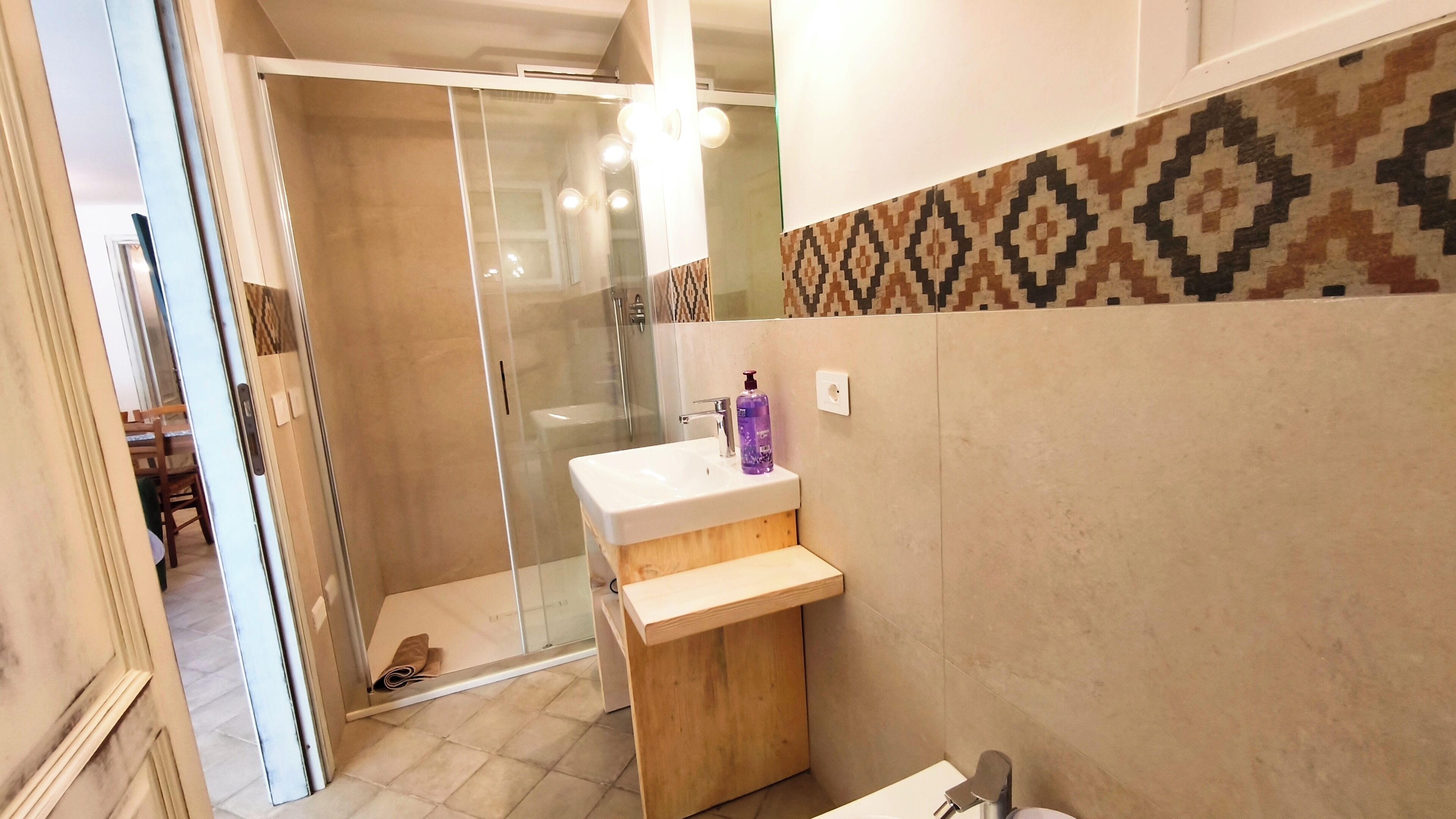 Un bagno con box doccia in vetro, lavabo con mobile contenitore in legno e piastrelle decorate.