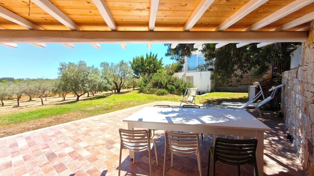 An outdoor patio with a table and chairs, a pergola, and a view of an olive grove. - Villa Teria, exclusive property! (Santa Maria Navarrese)