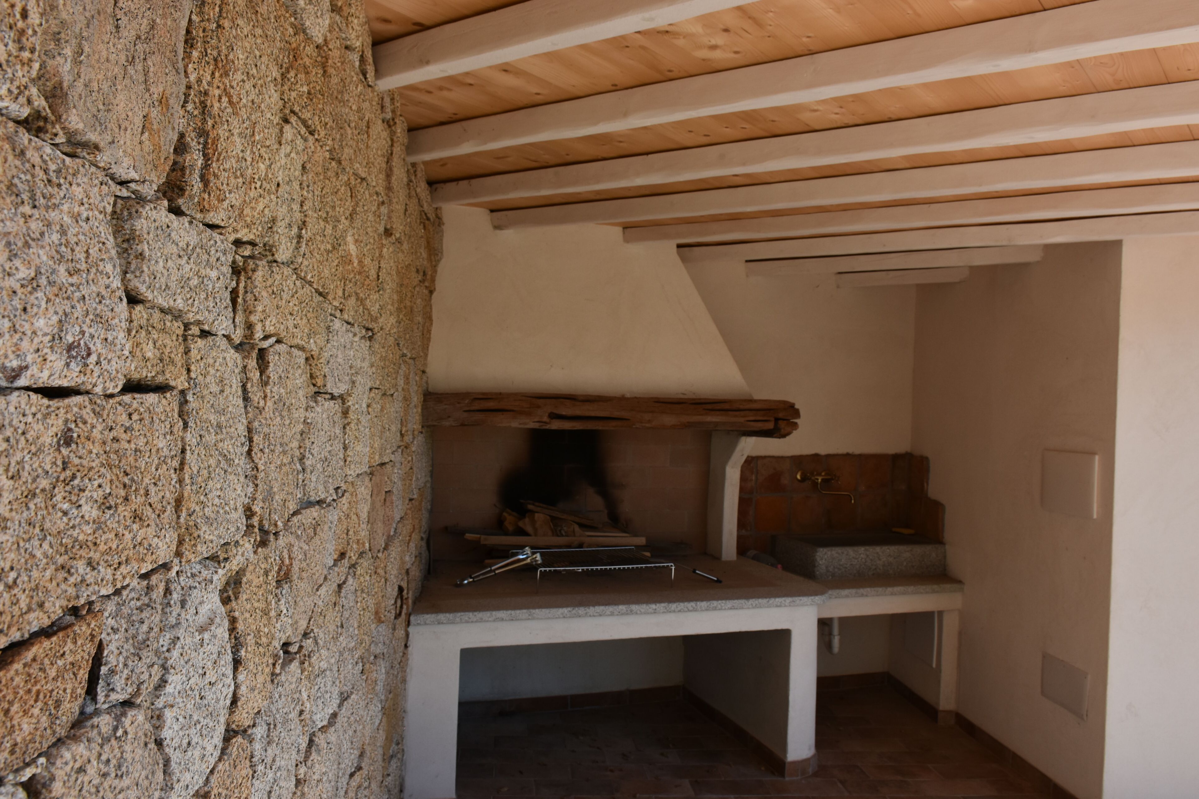 Una pared de piedra, techo de madera y un banco con chimenea.