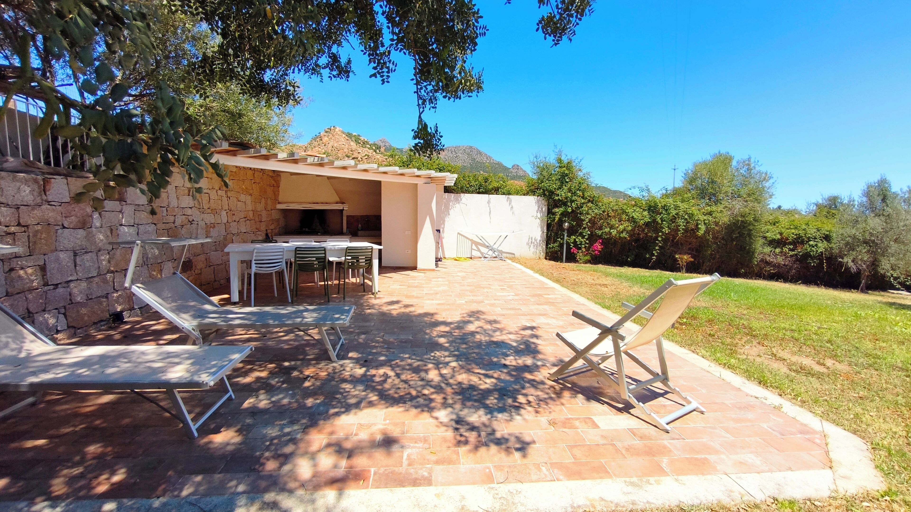 Un patio exterior con pared de piedra, una parrilla y mobiliario.