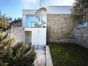 A modern building with a spiral staircase, a stone wall, and a small garden area. - Villa Teria, exclusive property! (Santa Maria Navarrese)