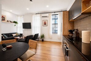 Een moderne woonkamer met een bank, eettafel, stoelen, een flatscreen-tv en een keuken met een fornuis en kastjes.