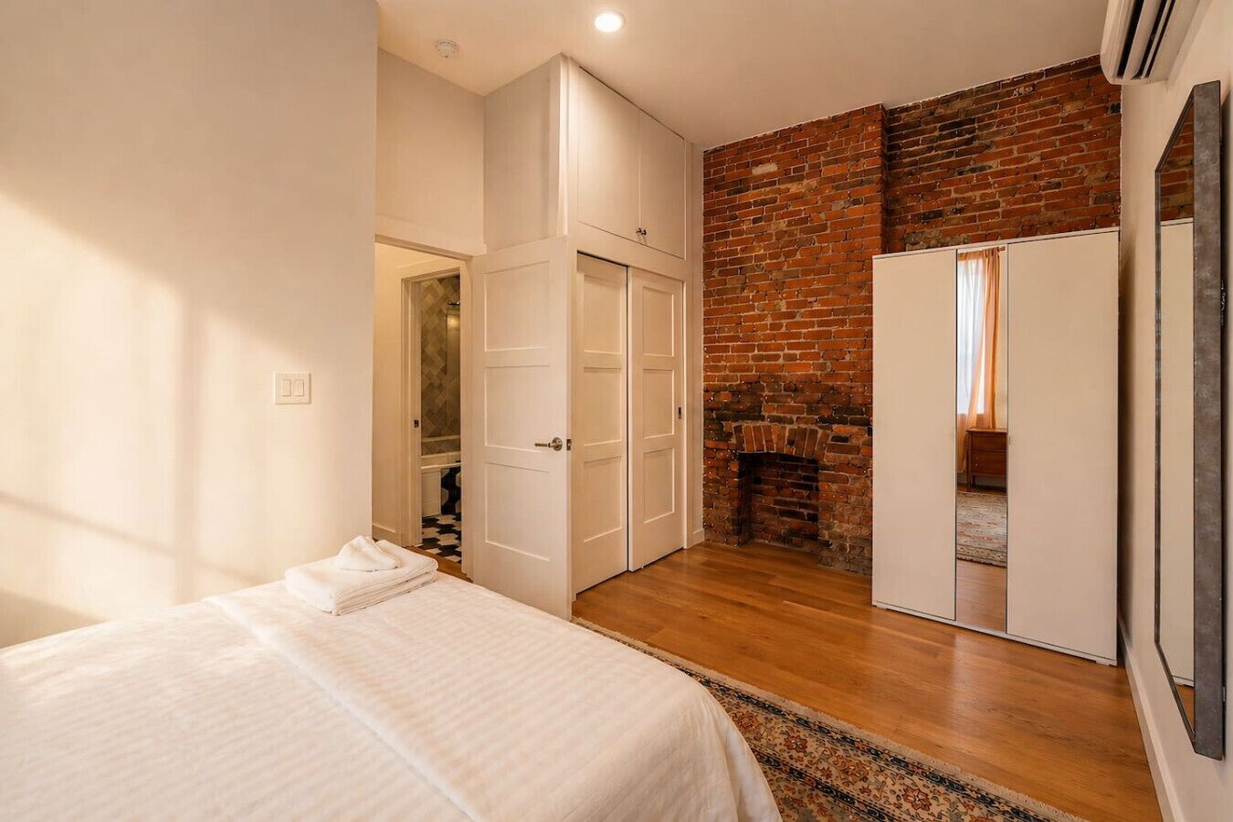 A bedroom with a bed, a wardrobe, a mirror, and a brick wall.