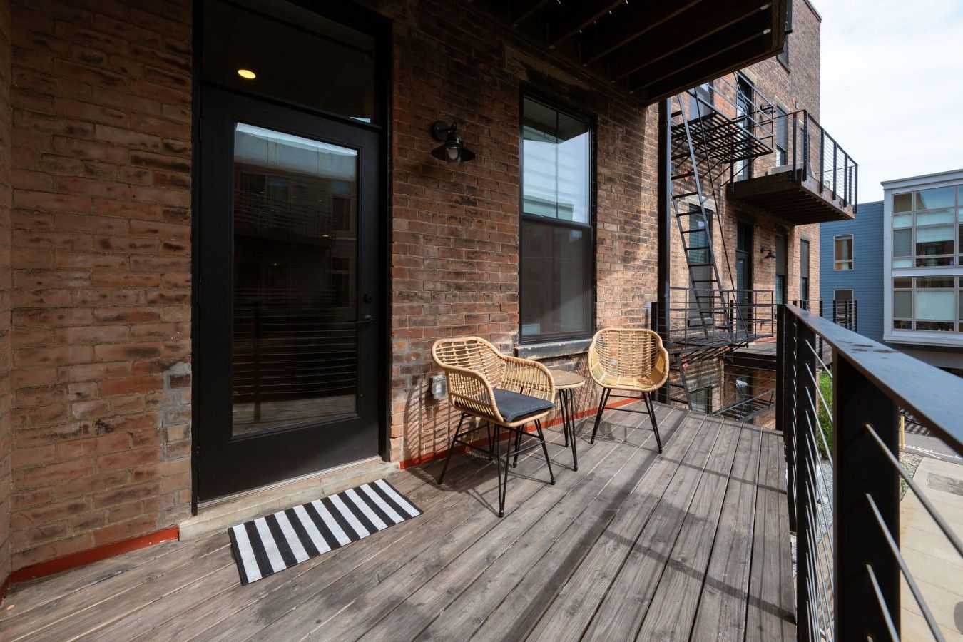 Een houten terras met twee rieten stoelen en een zwarte metalen balustrade.