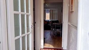 Un couloir recouvert d’une moquette rouge, un coin repas avec une table et des chaises, et une porte dotée de panneaux de verre.