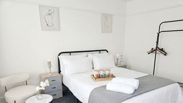 Une chambre bien rangée, avec un lit, des tables de chevet, une chaise et des œuvres d’art accrochées aux murs.