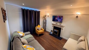 Un salon comprenant un canapé, un petit fauteuil, une cheminée et un téléviseur.