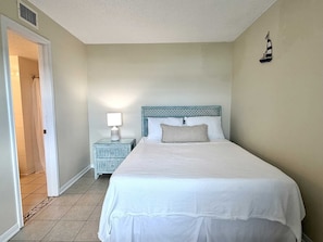 A bedroom with a bed, a nightstand with a lamp, a door, and a wall-mounted sailboat decoration.