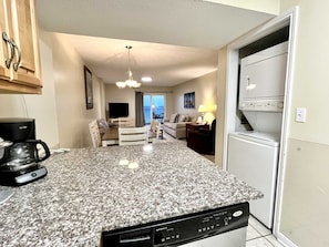A kitchen with granite countertops, a coffee maker, a dishwasher, and a dining area with a table and chairs.