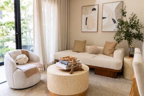 Een moderne woonkamer met een bank, fauteuil en een rond bijzettafeltje, met boeken en een decoratief object.