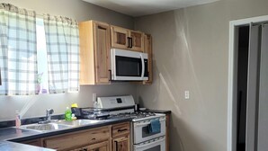 Une cuisine avec des meubles de rangement en bois, un four à micro-ondes, une cuisinière et un ventilateur de plafond.