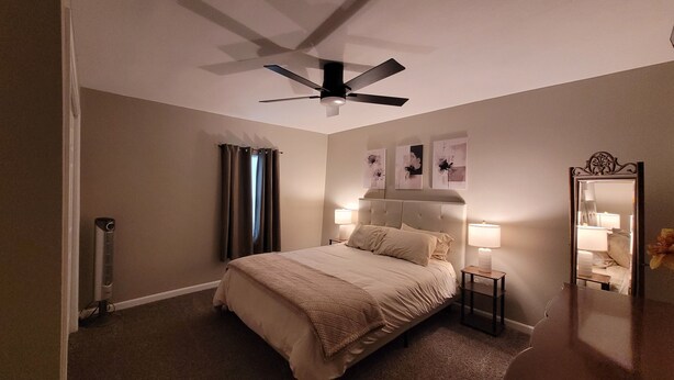 Une chambre à coucher comprenant un lit, un ventilateur de plafond, un radiateur, un miroir et des œuvres d’art mural.