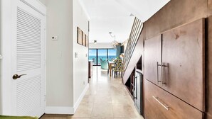 A hallway with a white door, a wooden cabinet, and a dining area with a view. - The Coastal View Gulf Front Condo in Seagrove Beach Sleeps 7 with a Pool (Santa Rosa Beach)