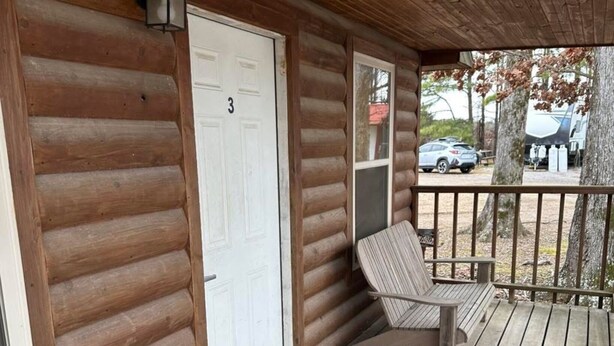 Une cabane en rondins avec un porche, une porte blanche portant le numéro 3 et un banc.