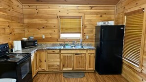 Une cuisine rustique, située dans une cabane en bois, équipée d’une cuisinière, d’un four à micro-ondes, d’un évier et d’un réfrigérateur noir.