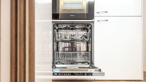 An open dishwasher with a control panel, a microwave above it, and a white cabinet to the right. - Apartment near the center and the sea, cozy for families and copies (San Benedetto del Tronto)