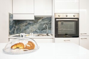 Una cucina moderna con schienale in marmo, elettrodomestici in acciaio inossidabile e una vetrina con pasticceria.