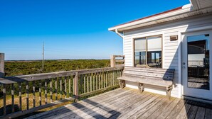 A wooden deck with a bench, a white building with a window, and a view of greenery. - South Nags Head 4-Bedroom House Ocean & Sound Views  Hot Tub and Community Pool (Nags Head)