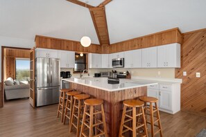 Een moderne keuken met een groot eiland, houten details, roestvrijstalen apparatuur en barstoelen.