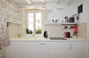 Eine Küche mit weißen Schränken, einer Steinwand, einem Fenster mit Aussicht und verschiedenen Küchengeräten.