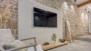 Ein modernes Wohnzimmer mit Steinwand, einem Wand-Fernseher, einer Holzleiter und einem gepolsterten Sessel.