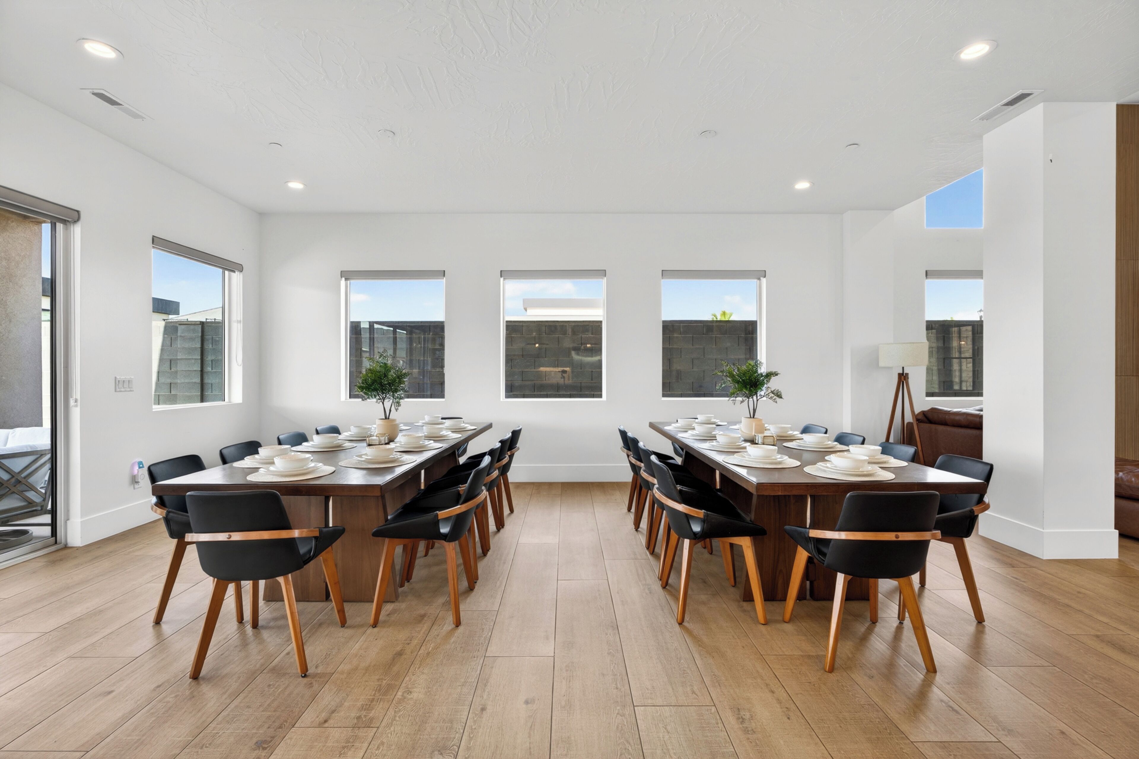 A modern dining room with a long table, black chairs, and potted plants.