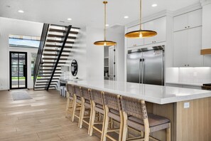 A modern kitchen with a central island, stainless steel appliances, and a wooden staircase. - Spacious 7 Bed Private Pool + Pickleball (Hurricane)
