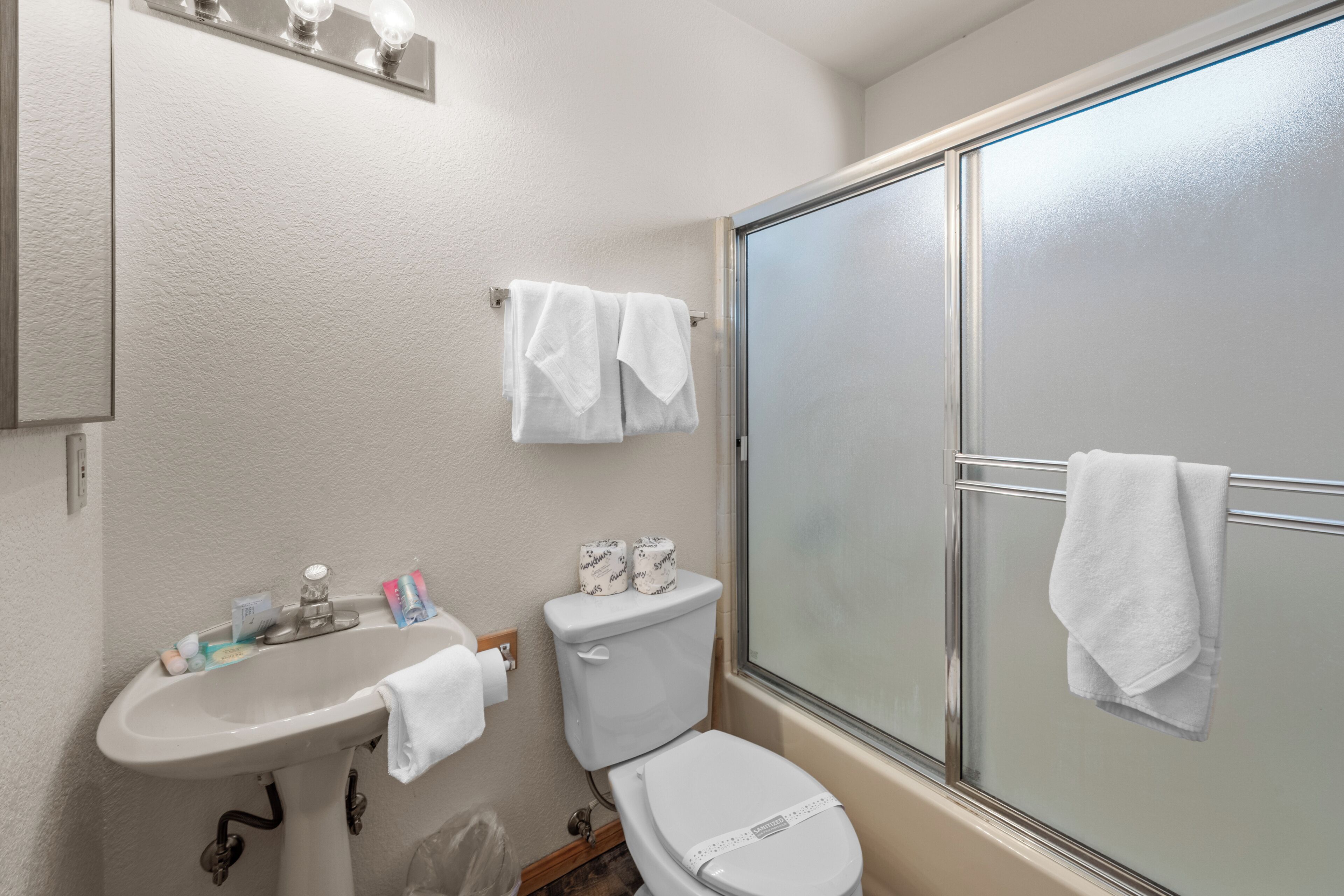 A bathroom with a sink, toilet, and shower. There are towels hanging on the wall and a mirror above the sink.