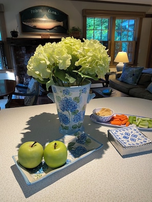A kitchen counter with a vase of flowers, two apples, a plate with vegetables, and a decorative plate with a blue pattern.