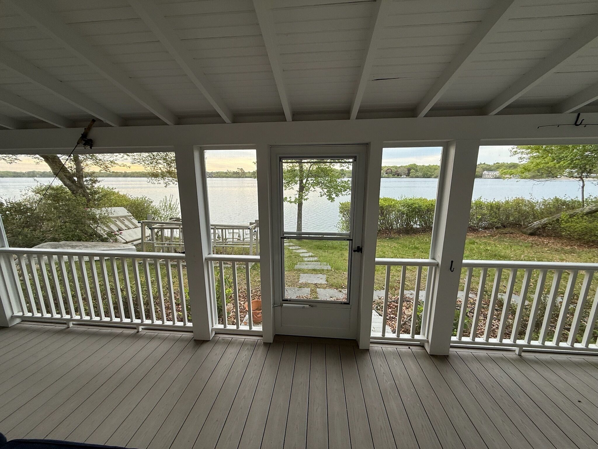 A covered porch with a view of a lake and a house across the water.