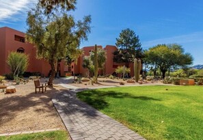 A courtyard with a paved walkway, surrounded by cacti and trees, leading to a building with a red facade. - CASA GINA - Anasazi Village - Pool View (Phoenix)