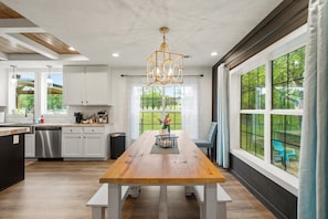 A modern kitchen with white cabinets, a wooden dining table, and large windows with curtains. - Animals, Hot Tub, Fire Pit, Museum in Hot Springs! (Hot Springs)