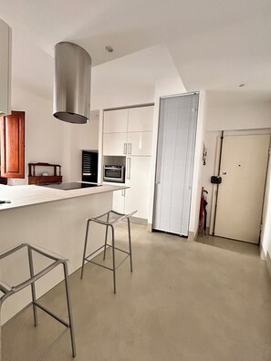 A modern kitchen with a central island, a built-in oven, and a stainless steel range hood. There are two metal bar stools and a wooden cabinet. - Casa Aligi by FlorenceHospitality (Firenze)