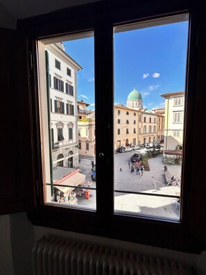 A window with a view of a city square, buildings, and a green dome structure. - Casa Aligi by FlorenceHospitality (Firenze)