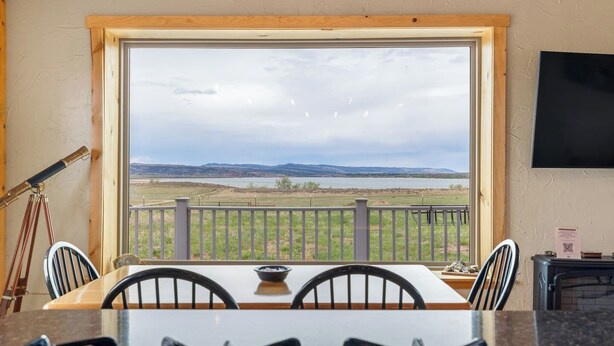 Un espace repas comprenant une table et des chaises, un télescope et une vue sur un paysage, visible à travers une grande fenêtre.