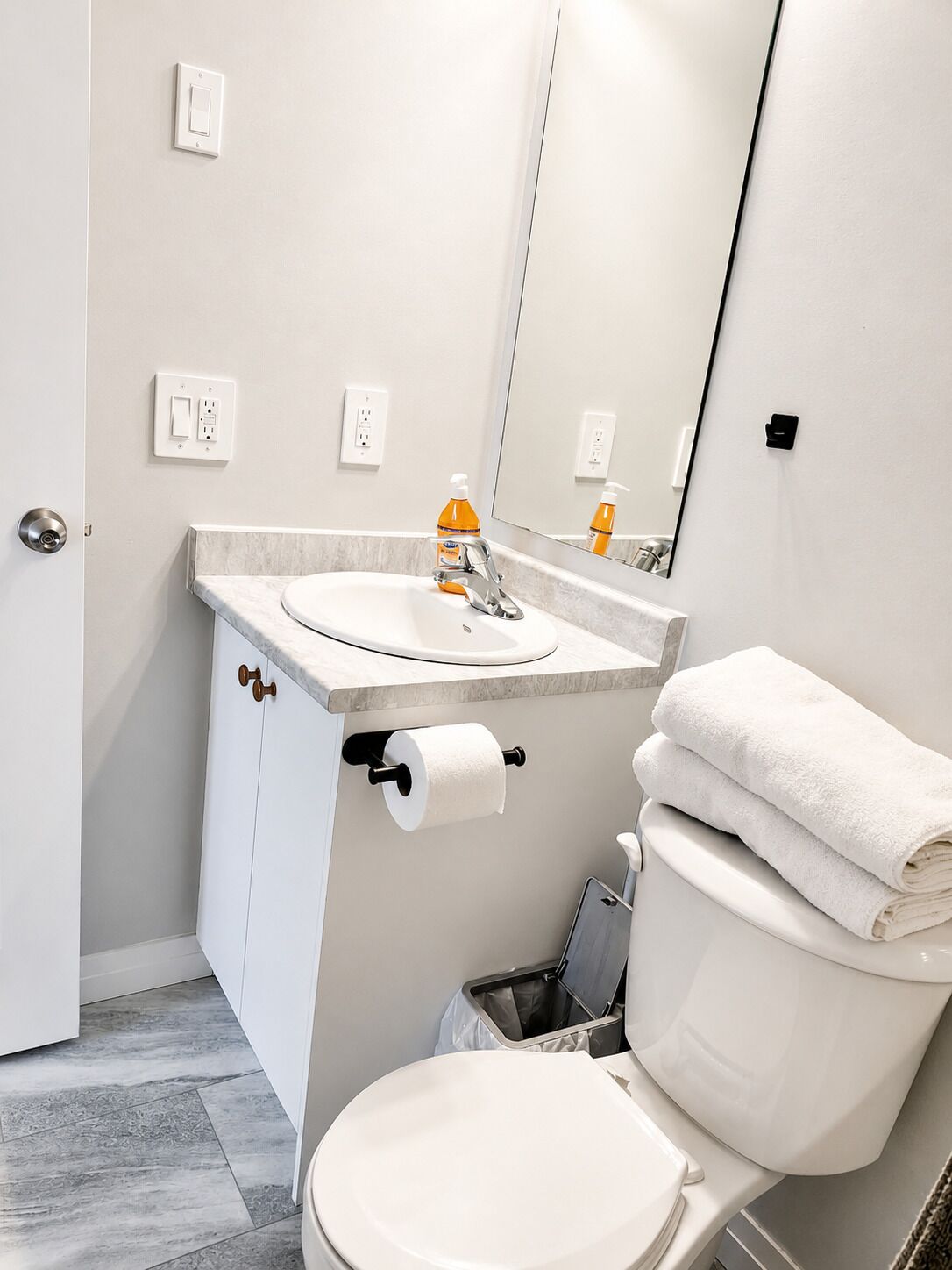 Et badeværelse med toilet, vask, spejl og håndklædetørrestativ.